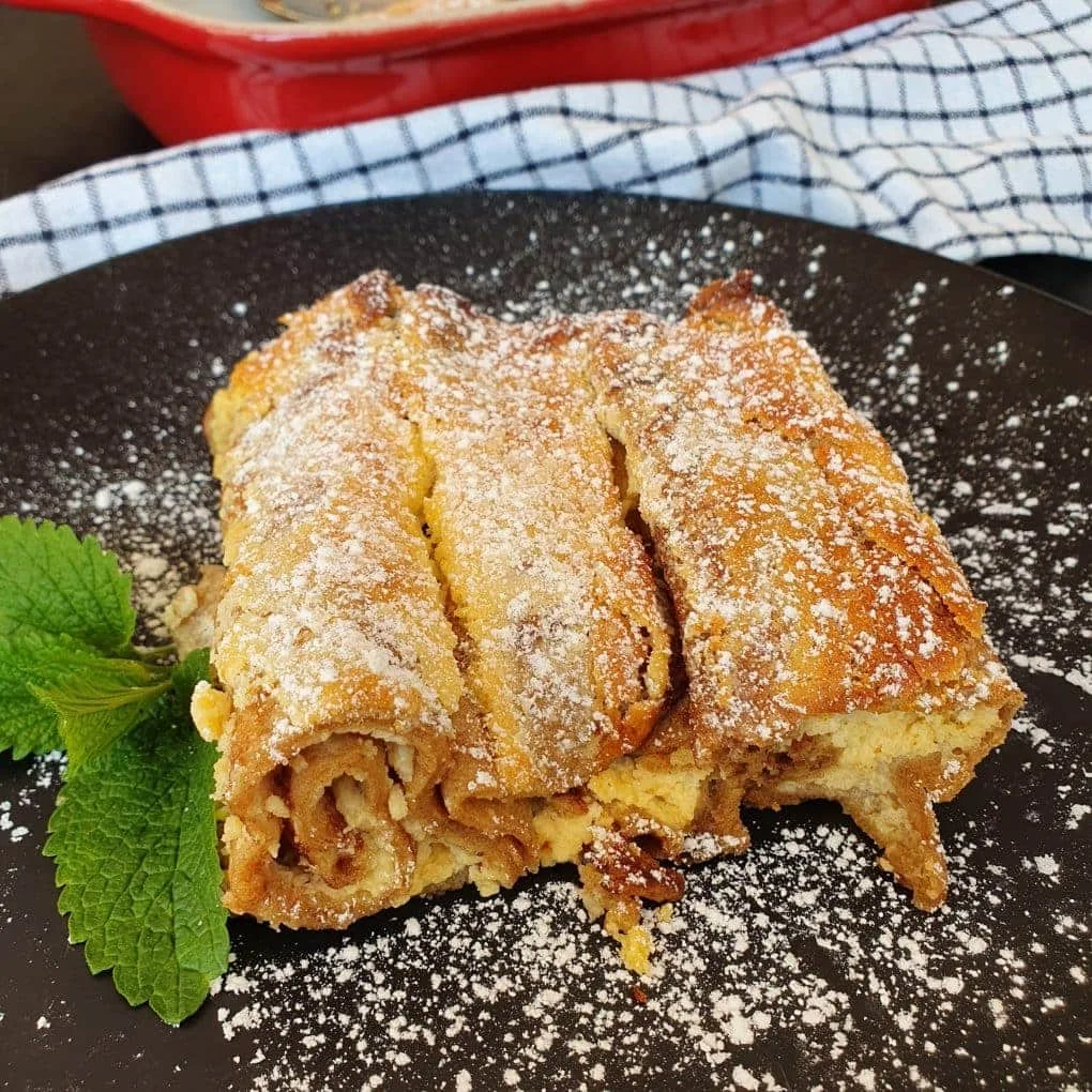 gefüllte Pfannkuchen mit grünem Blatt auf schwarzem Tellser. Dahinter ein Stück einer roten Schale