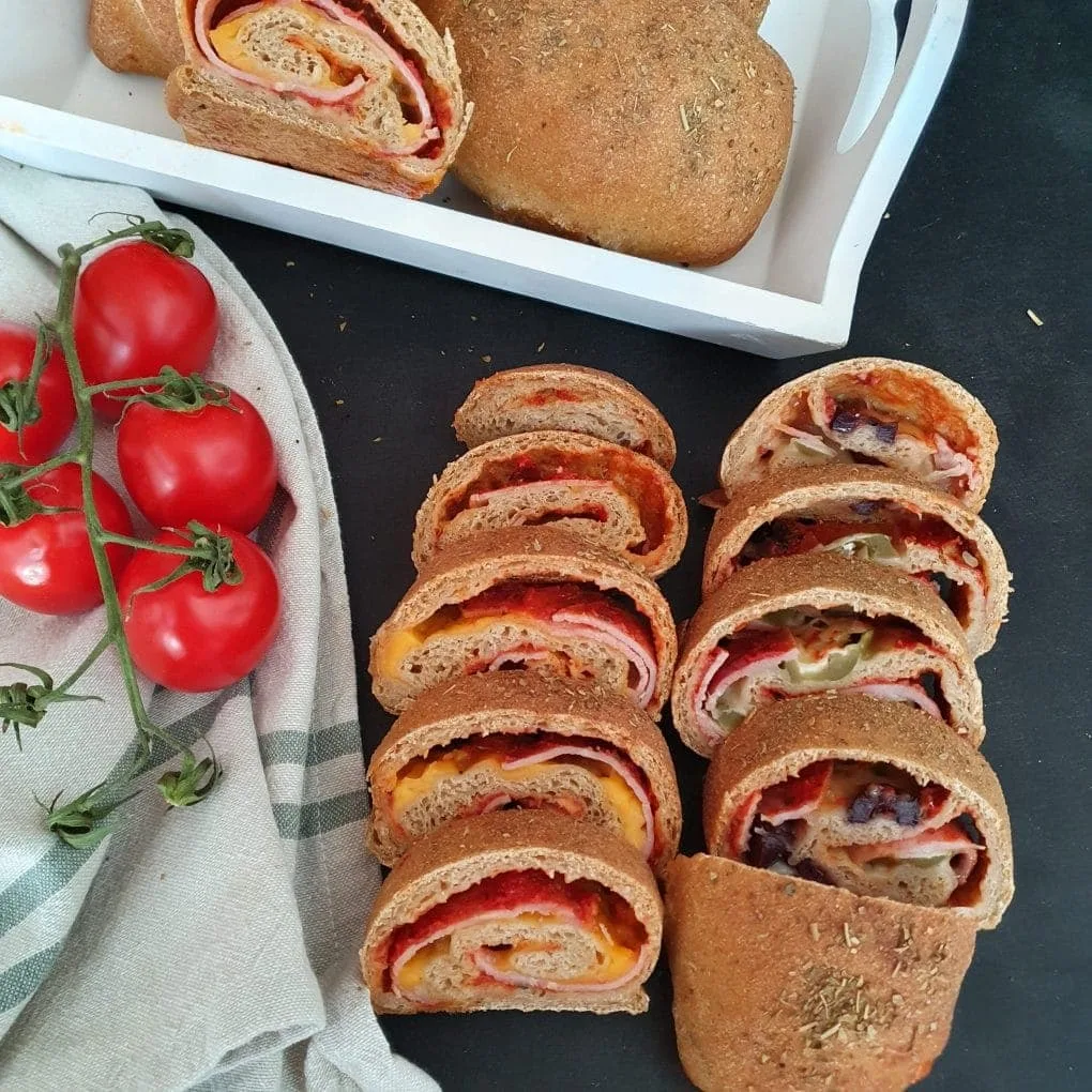 gebackene und gefüllte Brötchen in Scheiben geschnitten. Daneben Tomaten und weißes Tablett dahinter
