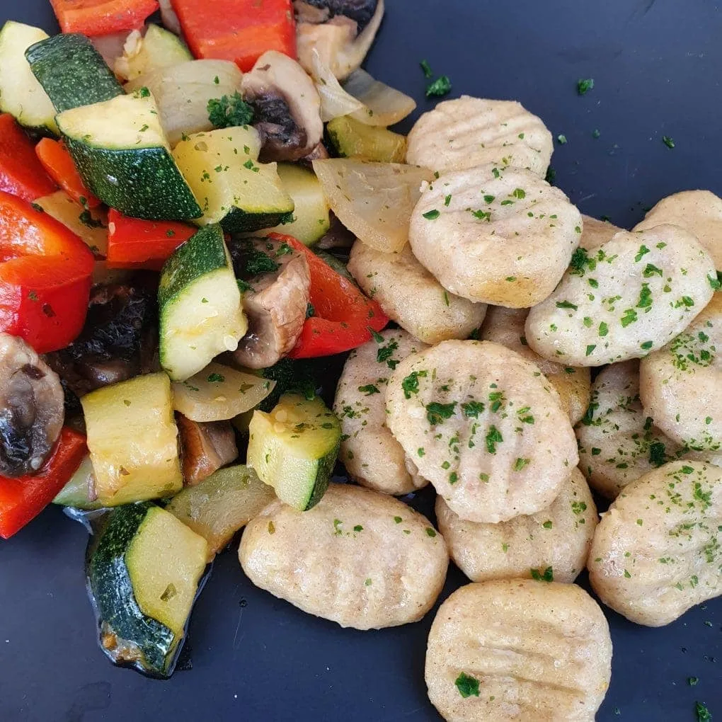 Gnocchi mit buntem Gemüse auf schwarzem Teller
