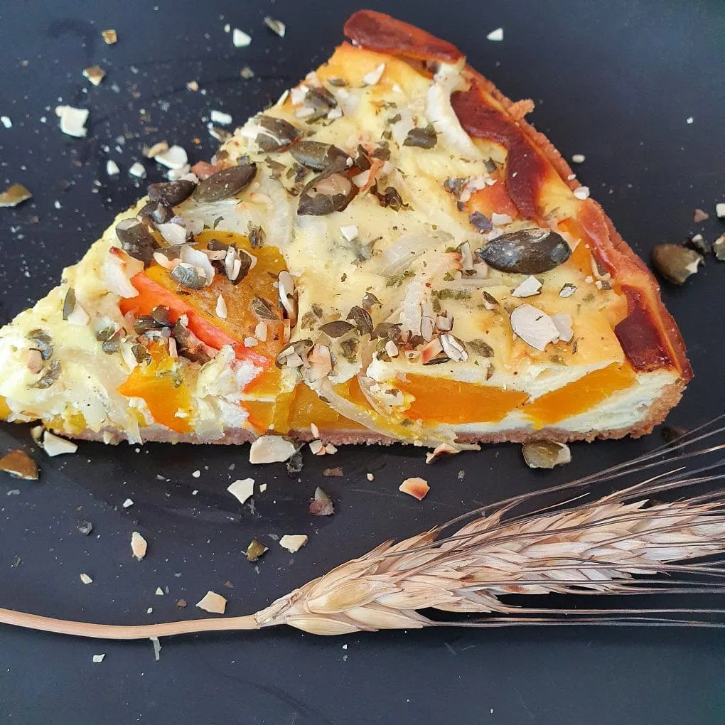 ein Stück Kürbis-Tarte mit Khorasan auf einem schwarzen Teller. Daneben eine Getreideähre