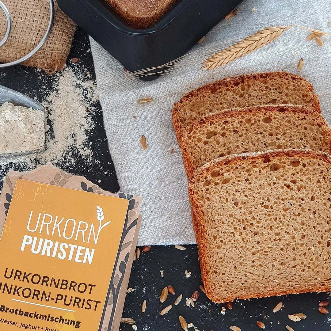 3 Scheiben Brot vom EinkornPurist aufgeschnitten. Daneben die leere Packung und diverse Deko passend zum Brotbacken