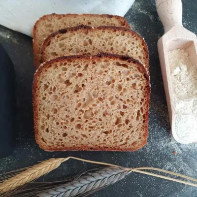 drei Scheiben Urkornbrot mit Senf-Sesamkruste mit Mehlschippe und Ähren
