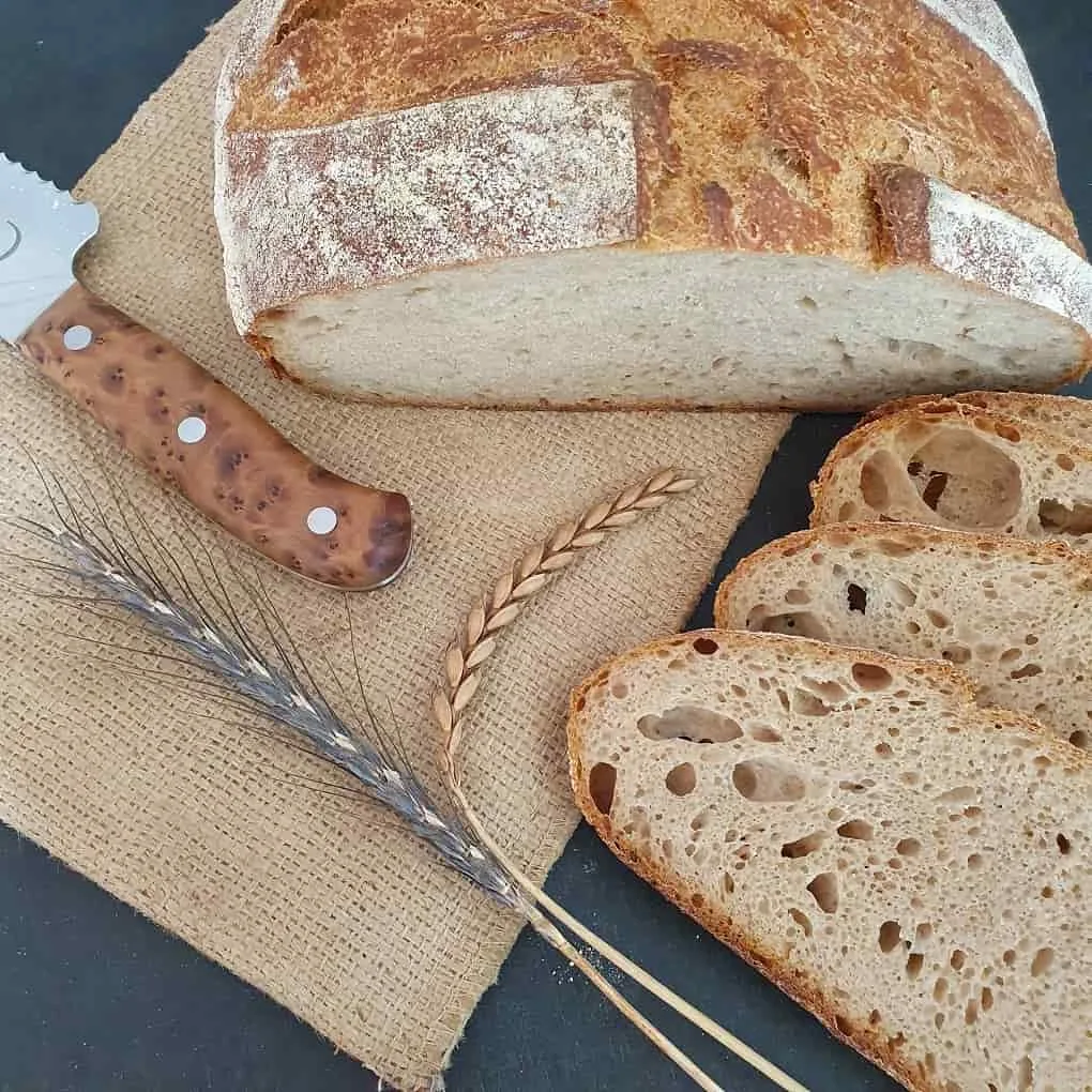 angeschnittenes Dinkelbrot 50% Vollkkorn auf schwarzem Tisch mit Ähren und Brotmesser