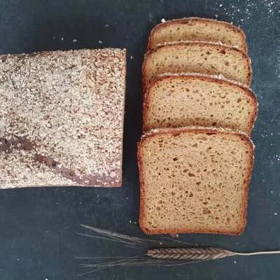 Einkorn Vollkornbrot mit Buttermilch und Kartoffeln. aufgeschnitten auf schwarzem Tisch. Daneben liegt eine Einkornähre
