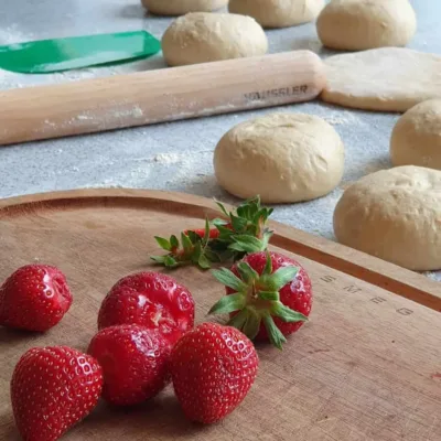 Erdbeeren auf Schneidebrett. Im Hintergrund Teiglinge