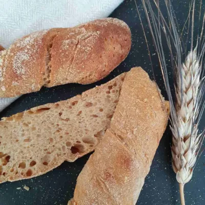 Khorasan Weißweinstangen aus 100% Vollkorn liegen auf schwarzem Tisch. Daneben eine Getreideähre vom Khorasan