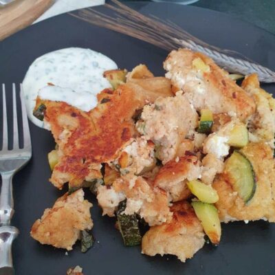 Zucchini Schmarrn auf schwarzem Teller mit Gabel und Joghurt Dipp