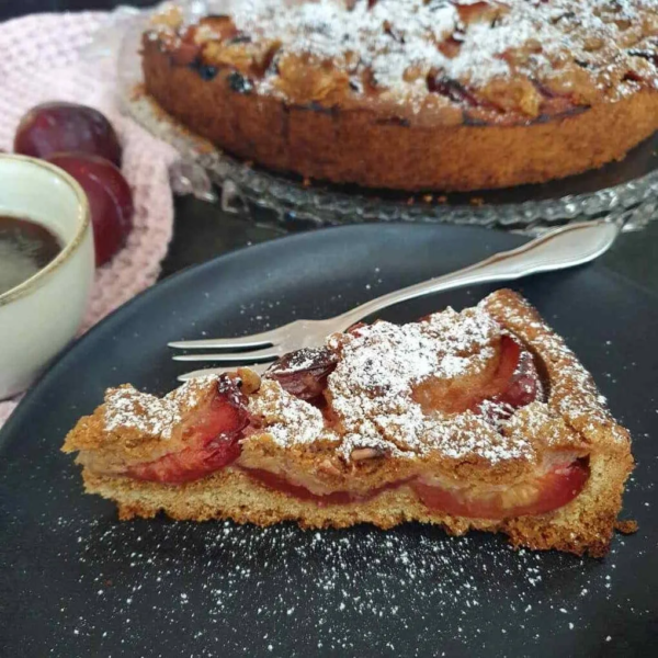 Pflaumenkuchen mit Einkorn und Streusel auf schwarzem Teller