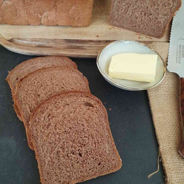 Vollkorntoast aus Rotkornweizen. Aufgeschnittene Toastbrotscheiben auf schwarzem Tisch. Daneben ein stück Butter