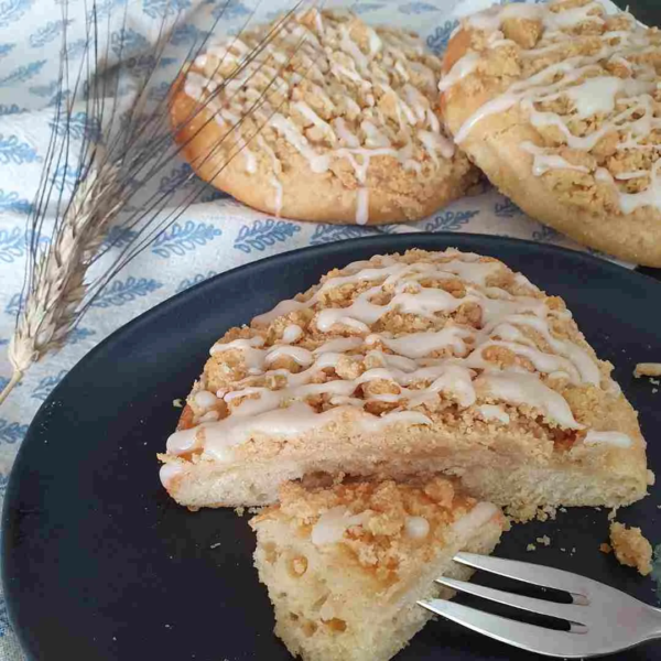 Khorasan Streuseltaler auf schwarzem Teller serviert. Im Hintergrund weiteres Gebäck und eine Khorasan Ähre