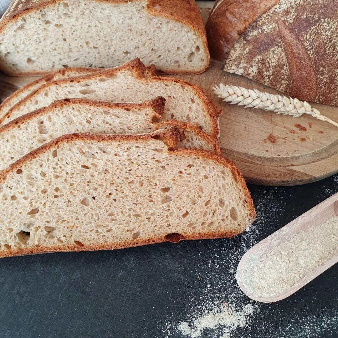 4 Scheiben Gelbmehlweizen all in one aufgeschnitten auf dem Tisch. Mehlschaufel aus Holz, Holzbrett
