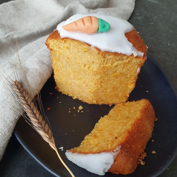 Einkorn Rüblikuchen im Weckglas mit weißer Glasur auf schwarzem Teller. Getreideähre, Tuch daneben