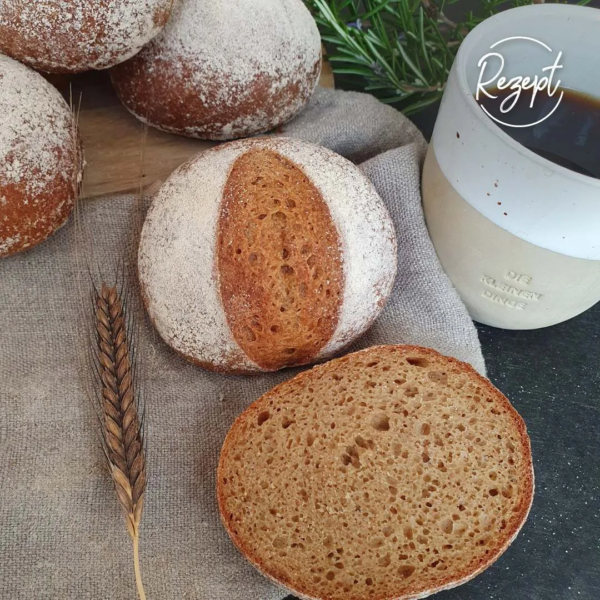 Einkornbrötchen Version II einfacher - aufgeschnitten neben Kaffeetasse. einkornähre Tuch, grüner Zweig am Bildrand