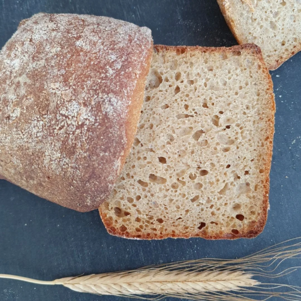 Nahaufnahme eines aufgeschnittenen Einkornbrötchen Version III. Einkornähre zur Deko liegt daneben