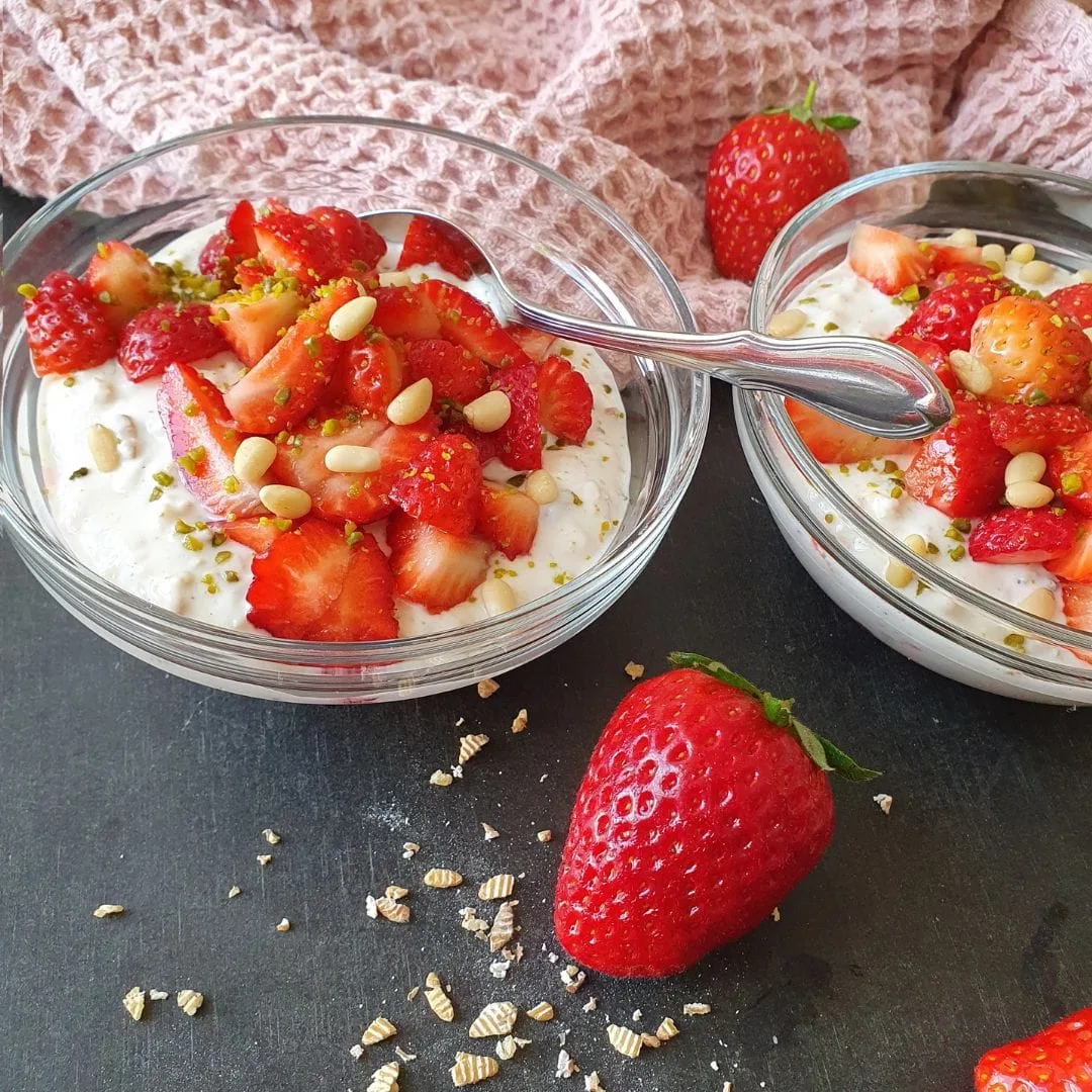 Erdbeer Urkorn Overnight servierfertig auf schwarzem Tisch. Erdbeere und rosa Tuch als Deko daneben