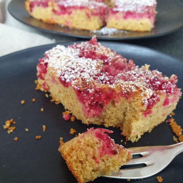 fruchtiger Einkorn Kuchen mit Johannisbeeren auf schwarzem Teller mit Kuchengabel