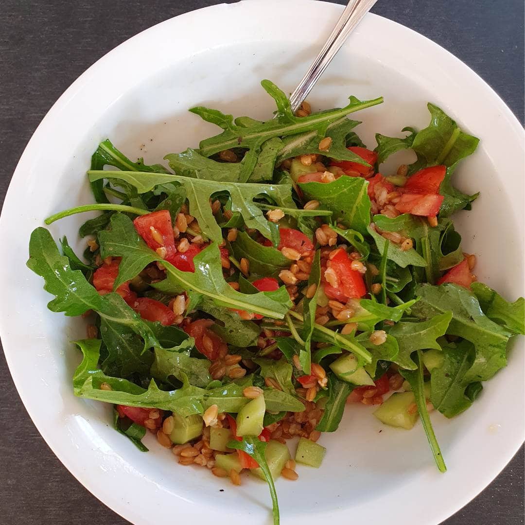 Sommersalat mit Einkorn in einer weißen Servierschüssel auf schwarzem Tisch