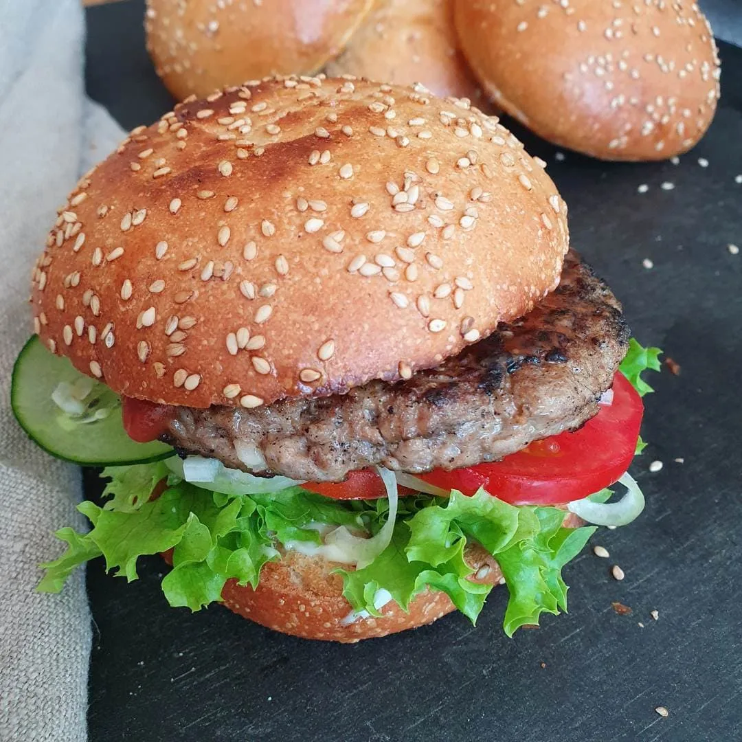 Hamburger fertig belegt mit Pattie, Tomaten, Salat, Gurke. Serviert auf schwarzem Teller