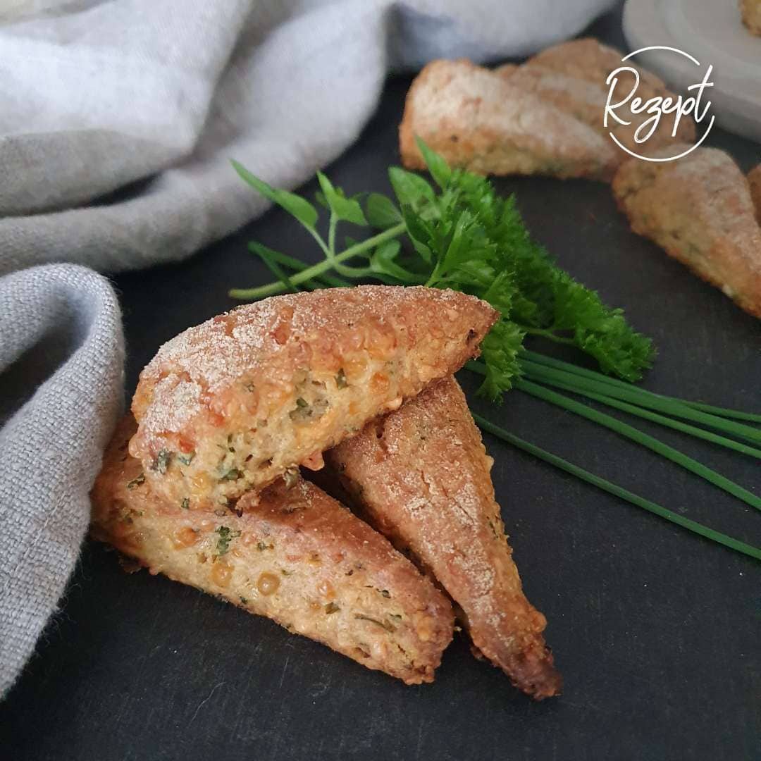 Scones aus Einkorn mit Käse und Kräuter. Mit Kräuter deko. Daneben ein Tuch. Scones liegen auf schwarzem Tisch fertig zum servieren