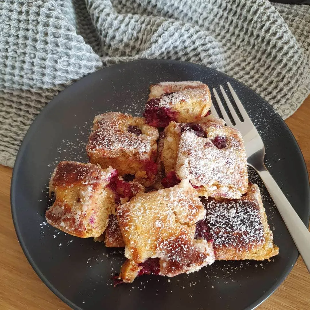 Brombeerküchlein auf schwarzem Teller. Graues Dekotuch daneben