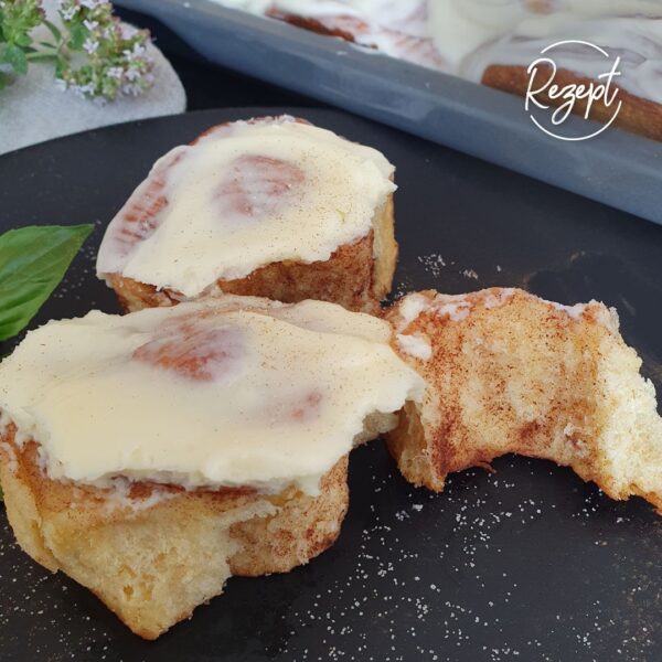 Zimtschnecke mit Frosting auf schwarzem Teller