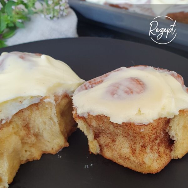 Zimtschnecken mit Frosting. aufgebrochen auf schwarzem Teller