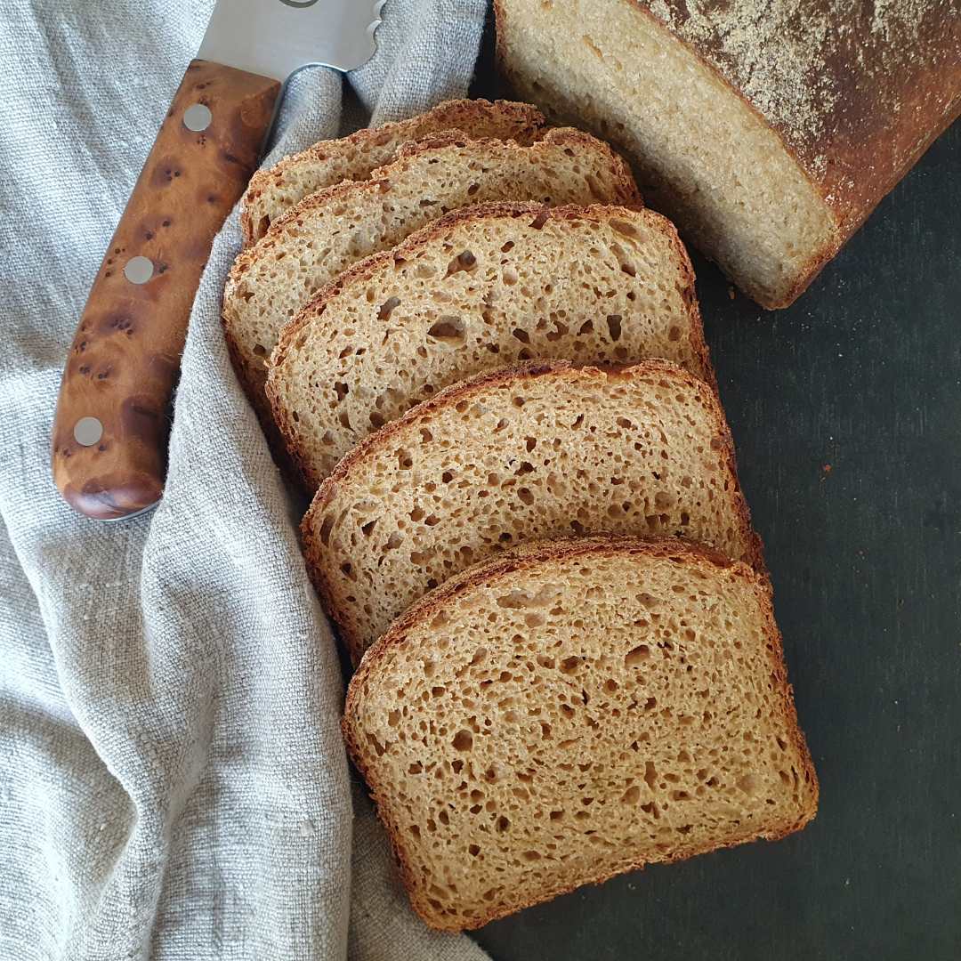 vier Scheiben Zucchini Kastenbrot aufgeschnitten auf schwarzem Tisch. daneben graues Tuch und Brotmesser