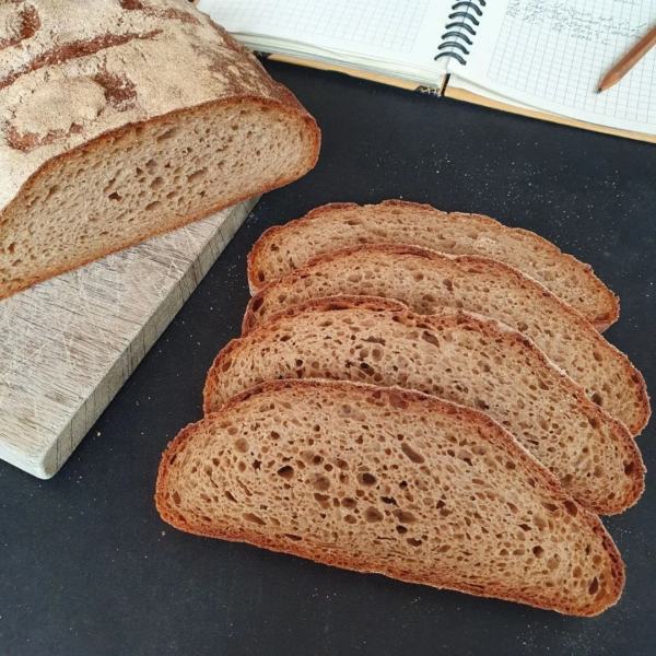 Urkorn Dreierlei aufgeschnitten auf schwarzem Tisch. Teil eines Notizbuches daneben