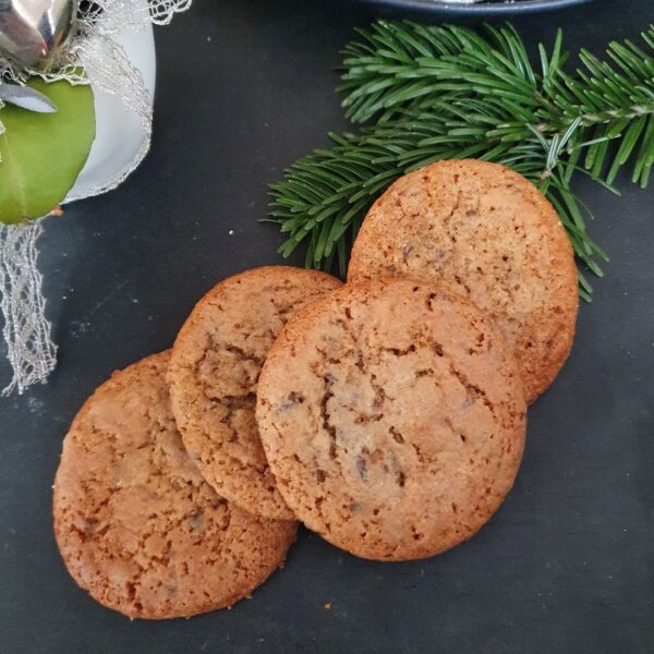 Aprikosen Gingerbread Plätzchen auf schwarzem Untergrund. Daneben Tannenzweig und Weihnachtsdeko