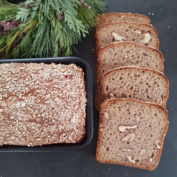 Winterbrot mit Walnüssen in Scheiben und in der Backform auf schwarzem Tisch. Daneben Deko aus Tannengrün