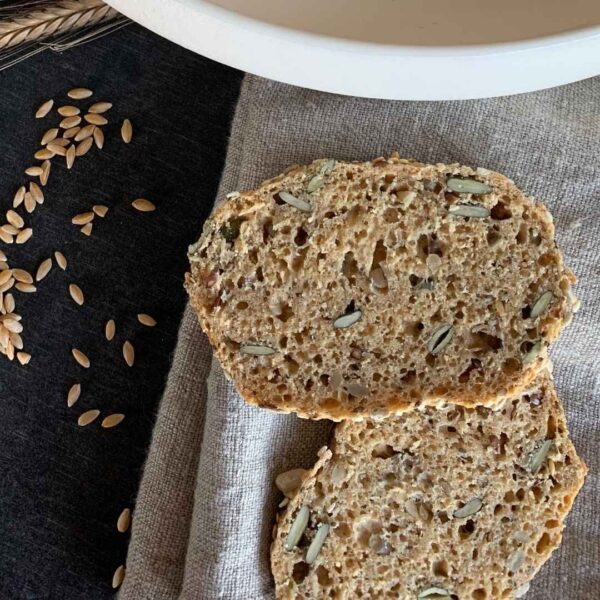 Urkornbrötchen mit Backpulver aufgeschnitten mit Schnittfläche nach oben liegen auf grauem Tuch. getreidekörner liegen auf schwarzem Tisch daneben