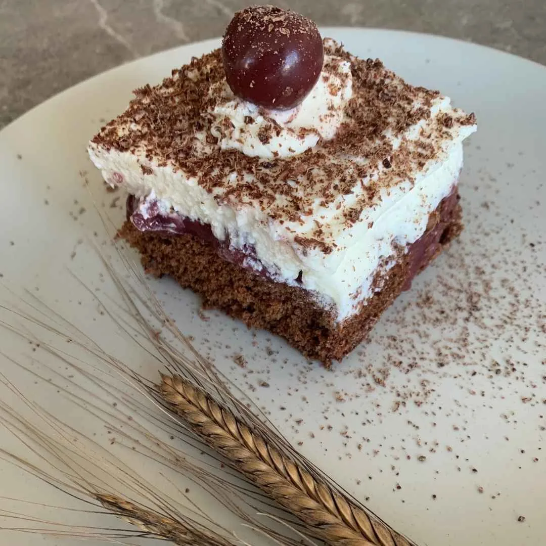Schwarzwälder Kirschschnitte auf beigen Teller. Daneben ein einkornähre