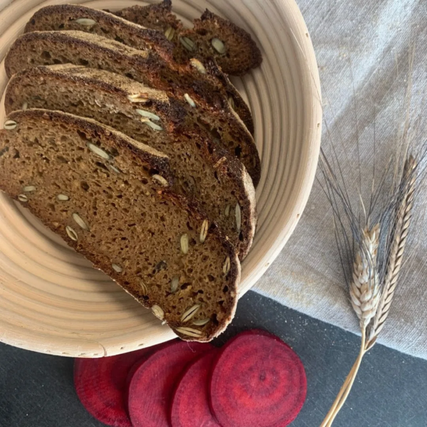 gesundes Vollkornbrot aus Brotbackmischung Buttermilchkruste mit Kürbiskernen und Roter Beete. In Scheiben geschnitten im Gärkörbchen, auf Leinentuch mit Roter Bete und Getreideähren