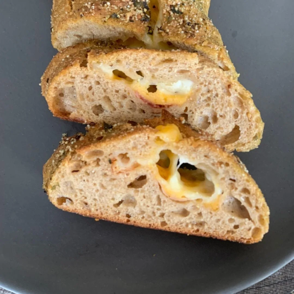 aufgeschnittene Brotscheibe von BlueVelvet Käsestangen auf schwarzem Teller von oben. Krume und Füllung sichtbar