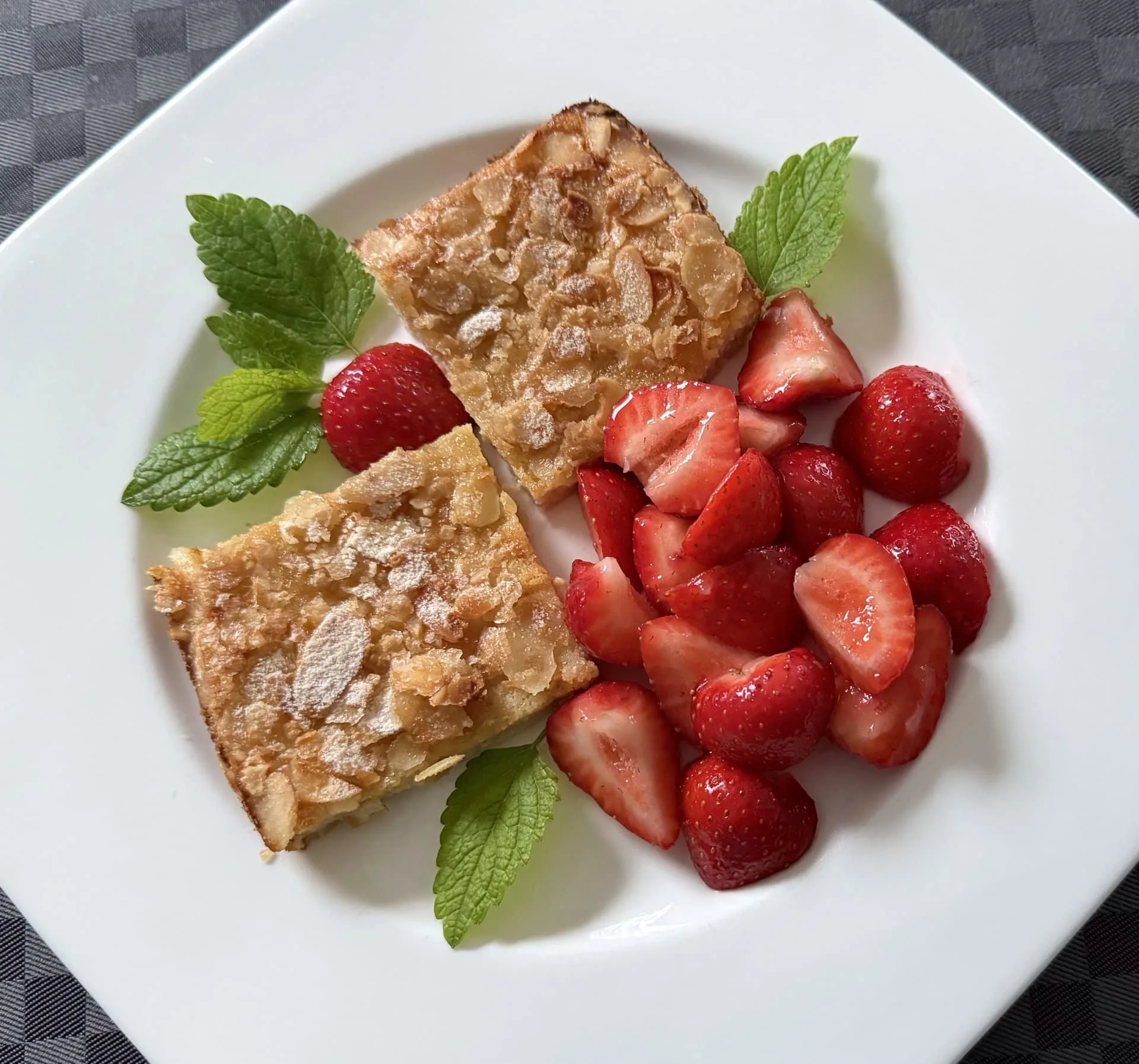 2 Stück Grießschnitten mit Khorasan liegen auf einem weißen Teller. daneben ein Salat aus Erdbeeren und Minzblättchen