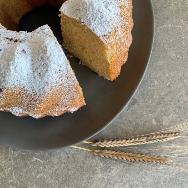Nahaufnahme Rührkuchen Gugelhupf aus Backmischung. angeschnitten. Ein Stück fehlt. Kuchen steht auf schwarzem Teller. Daneben liegen zwei Getreideähren