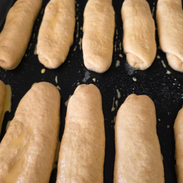 Hotdog Brötchen als Teiglinge auf einer schwarzen Backfolie