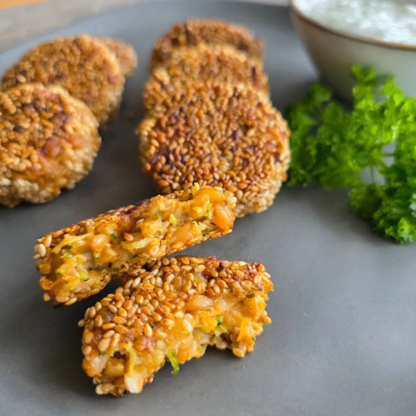 Nahaufnahme vegane Einkorn-Falafel. Im Vordergrund ist eine Falafel aufgebrochen, so dass das Innere zu sehen ist. Fünf Falafel sind im Hintergrund zusammen mit einem Stück petersilie zu sehen.
