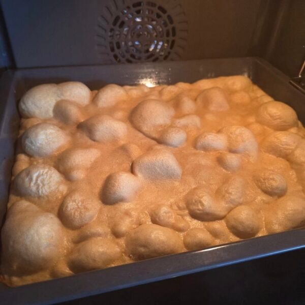 Ofenpfannkuchen halbgebacken im Ofen auf schwarzem Backblech. Teig wirft Blasen