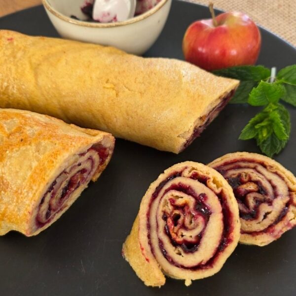 Ofenpfannkuchen aus Einkorn mit Marmelade gefüllt. Aufgerollt in Scheiben geschnitten. Auf schwarzem Teller zwei Rollen und 2 Scheiben angerichtet