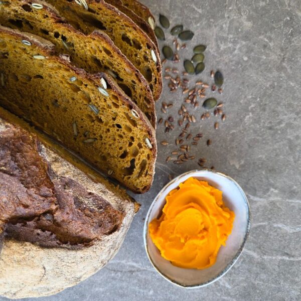 Herbstwald Brot mit Kürbis auf einer grauen Steinplatte. Drei Scheiben aufgeschnitten neben einem Brotlaib von oben. daneben liegen ein paar Kürbiskerne
