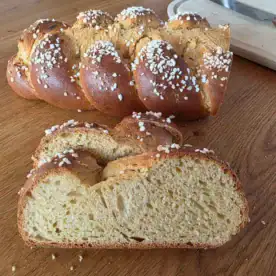 zwei scheiben Hefezopf liegen vor dem Laib Hefezopf auf einem Holztisch