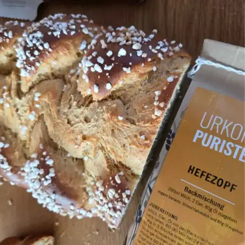 Ausschnitt von aufgerissenen Hefezopf von oben. daneben eine Packung der Backmischung für Hefezopf